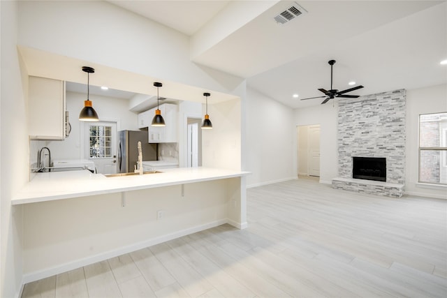 kitchen featuring kitchen peninsula, stainless steel fridge, decorative light fixtures, a breakfast bar area, and white cabinets