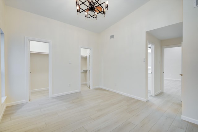 unfurnished bedroom featuring an inviting chandelier, light hardwood / wood-style floors, vaulted ceiling, a walk in closet, and a closet