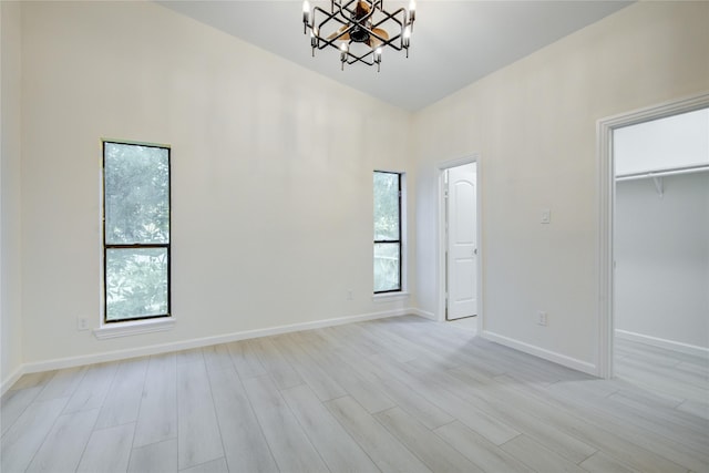 unfurnished bedroom with a notable chandelier, a walk in closet, light wood-type flooring, and a closet