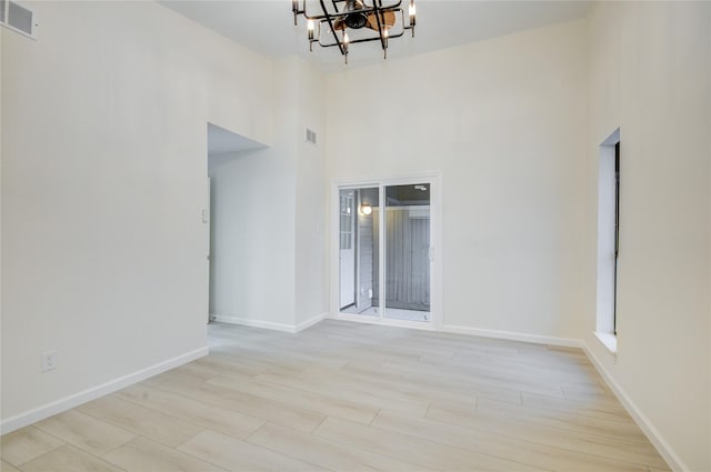 spare room featuring a chandelier, light wood-type flooring, and a towering ceiling