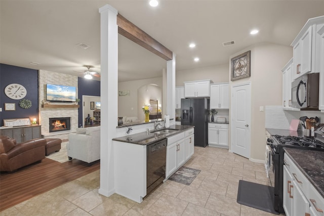 kitchen with black appliances, a stone fireplace, white cabinets, and sink