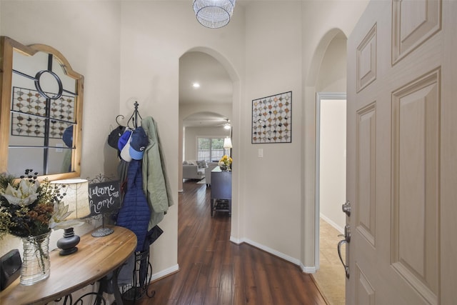 hallway featuring baseboards, arched walkways, wood finished floors, and a towering ceiling