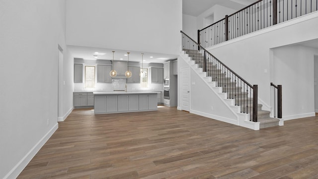 unfurnished living room featuring a towering ceiling, baseboards, dark wood-style floors, and stairs