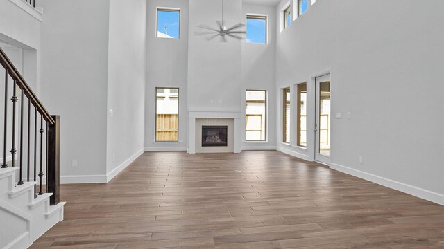 unfurnished living room featuring stairway, wood finished floors, baseboards, ceiling fan, and a glass covered fireplace