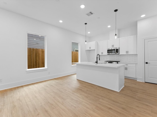 kitchen featuring white cabinetry, an island with sink, hanging light fixtures, and light wood-type flooring