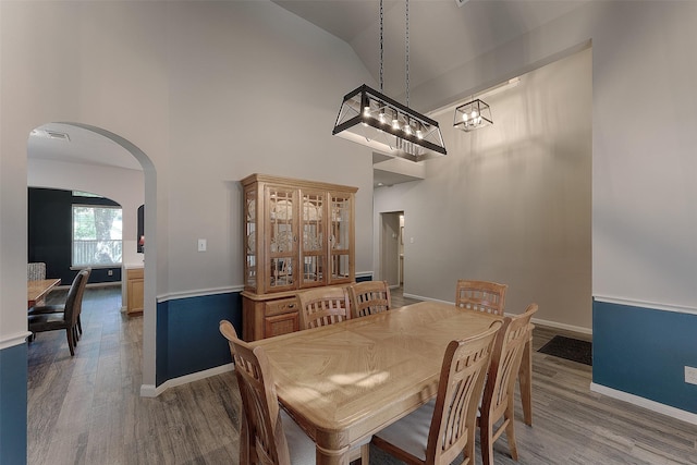 dining area with hardwood / wood-style flooring, high vaulted ceiling, and an inviting chandelier