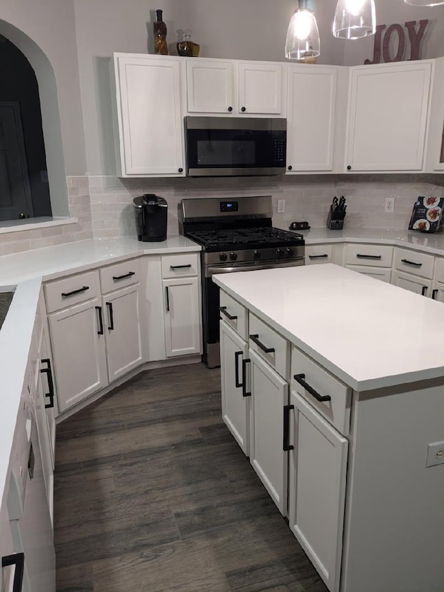 kitchen with appliances with stainless steel finishes, hanging light fixtures, decorative backsplash, white cabinets, and dark hardwood / wood-style floors