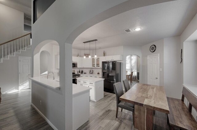 kitchen featuring light hardwood / wood-style flooring, pendant lighting, appliances with stainless steel finishes, white cabinetry, and a center island