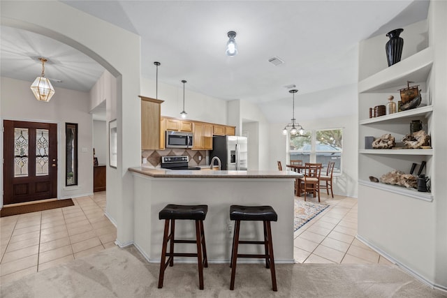 kitchen with decorative backsplash, light brown cabinets, decorative light fixtures, and appliances with stainless steel finishes