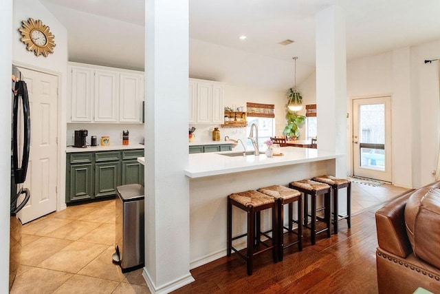 kitchen featuring sink, green cabinetry, a wealth of natural light, a kitchen bar, and white cabinetry