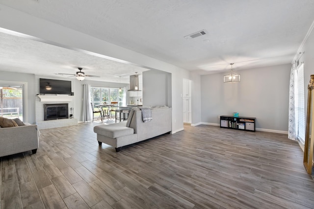 living room featuring a textured ceiling, a fireplace, wood-type flooring, and ceiling fan with notable chandelier