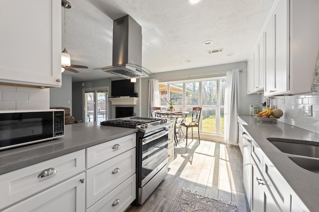 kitchen with white cabinets, decorative backsplash, ceiling fan, island range hood, and stainless steel range with gas stovetop