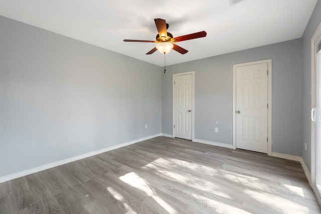 unfurnished bedroom with ceiling fan, light hardwood / wood-style flooring, and two closets