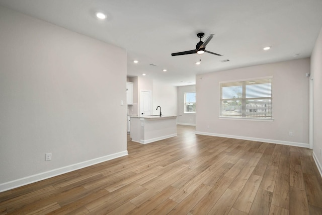 unfurnished living room featuring ceiling fan, light wood-type flooring, and sink