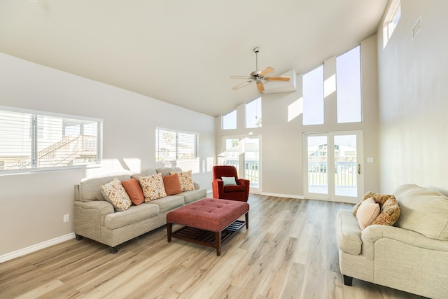 living room with ceiling fan, a towering ceiling, and light hardwood / wood-style floors