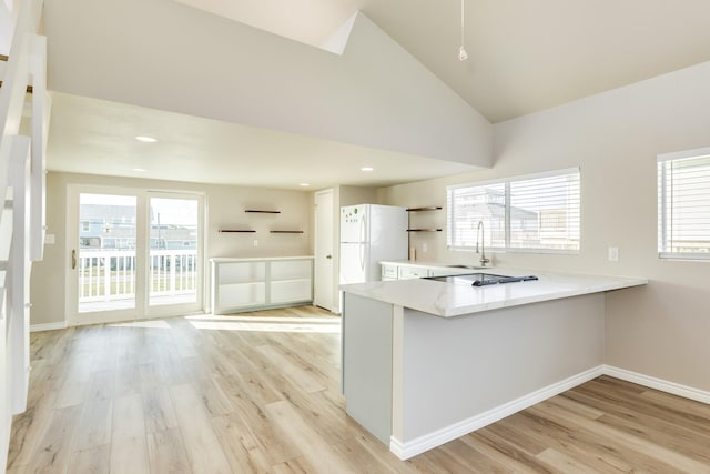 kitchen featuring sink, high vaulted ceiling, kitchen peninsula, white fridge, and light hardwood / wood-style floors