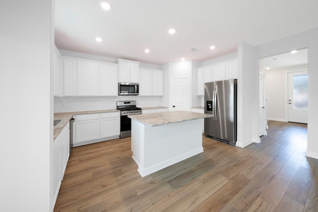 kitchen with light stone countertops, appliances with stainless steel finishes, light wood-type flooring, a center island, and white cabinetry