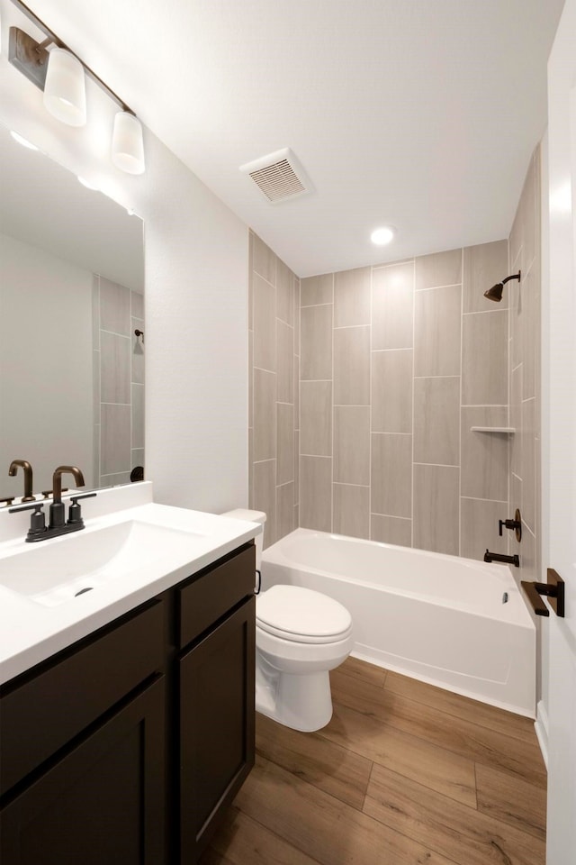 full bathroom featuring hardwood / wood-style flooring, vanity, toilet, and tiled shower / bath