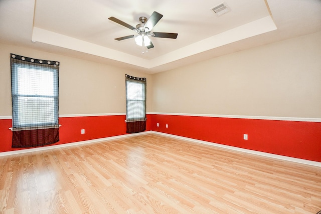 empty room featuring a raised ceiling, hardwood / wood-style floors, and a wealth of natural light