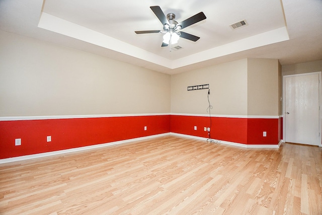 unfurnished room featuring ceiling fan, light wood-type flooring, and a tray ceiling