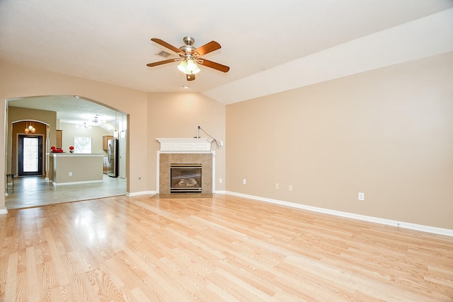 unfurnished living room with lofted ceiling, a tiled fireplace, ceiling fan, and light wood-type flooring