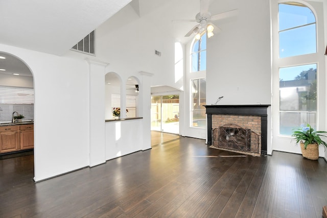 unfurnished living room with a towering ceiling, dark hardwood / wood-style flooring, a brick fireplace, and sink