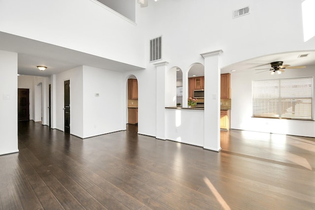 unfurnished living room featuring ceiling fan, dark hardwood / wood-style flooring, and a towering ceiling