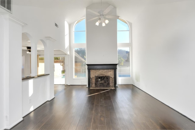 unfurnished living room with ceiling fan, a towering ceiling, dark wood-type flooring, and a brick fireplace