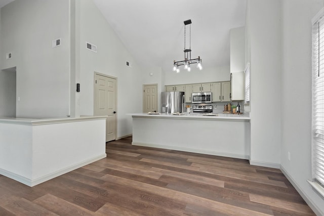 kitchen with high vaulted ceiling, appliances with stainless steel finishes, decorative light fixtures, dark hardwood / wood-style flooring, and kitchen peninsula