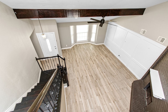 unfurnished living room featuring beamed ceiling, ceiling fan, and light wood-type flooring