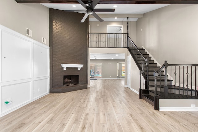 unfurnished living room featuring ceiling fan, a fireplace, beamed ceiling, and light hardwood / wood-style flooring