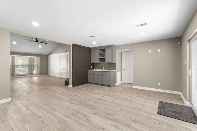 unfurnished living room featuring ceiling fan, sink, light hardwood / wood-style floors, and vaulted ceiling