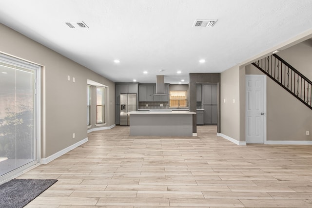 kitchen with a center island, backsplash, stainless steel refrigerator with ice dispenser, wall chimney exhaust hood, and gray cabinets