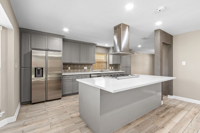 kitchen with stainless steel appliances, tasteful backsplash, island exhaust hood, gray cabinets, and a kitchen island