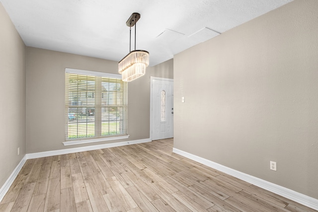 empty room featuring light wood-type flooring and a notable chandelier