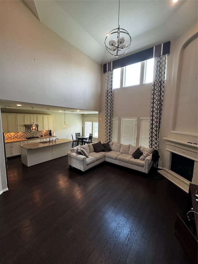 unfurnished living room featuring a fireplace, dark hardwood / wood-style flooring, high vaulted ceiling, and an inviting chandelier