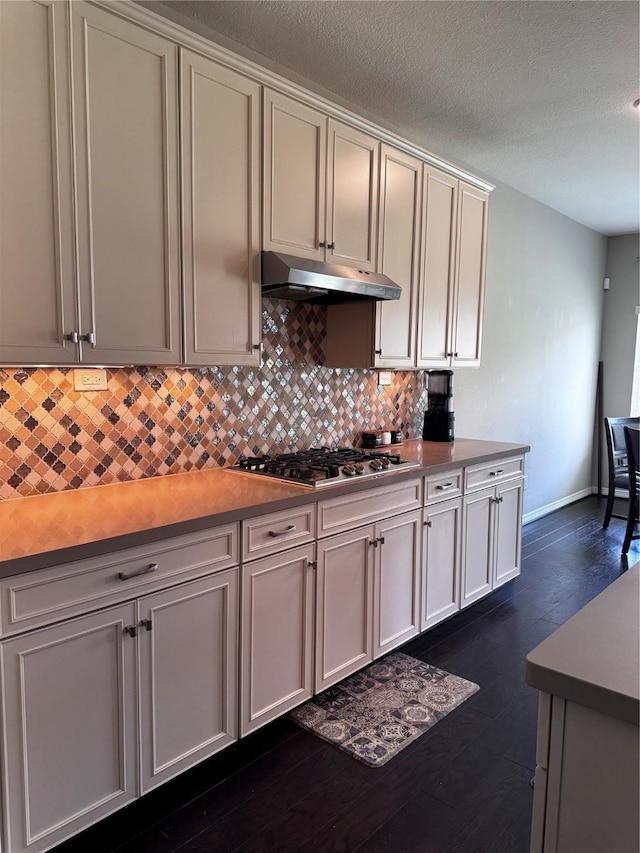 kitchen with a textured ceiling, dark hardwood / wood-style floors, stainless steel gas stovetop, and backsplash