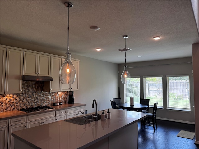 kitchen with sink, pendant lighting, stainless steel gas stovetop, decorative backsplash, and a center island with sink