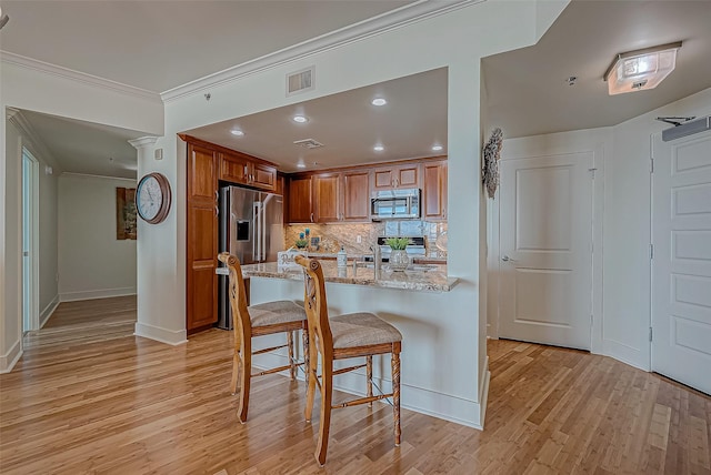 kitchen featuring light stone counters, a breakfast bar, brown cabinets, ornamental molding, and stainless steel appliances