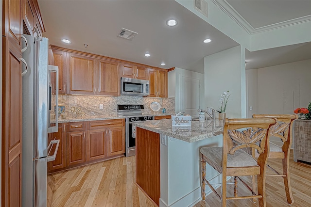 kitchen featuring light stone counters, visible vents, backsplash, appliances with stainless steel finishes, and light wood-type flooring