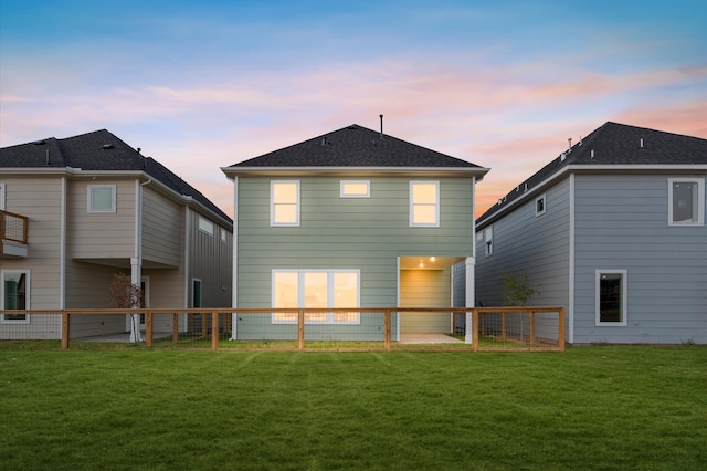 back house at dusk featuring a lawn