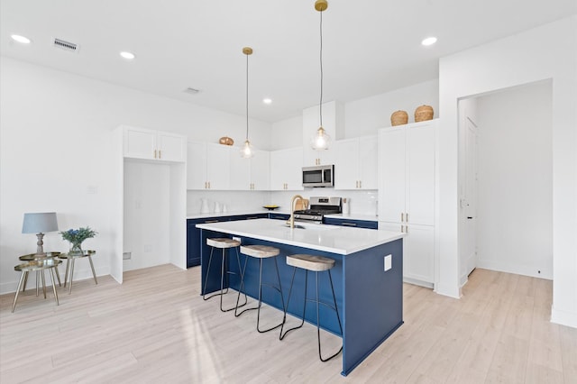 kitchen featuring backsplash, an island with sink, pendant lighting, white cabinets, and appliances with stainless steel finishes