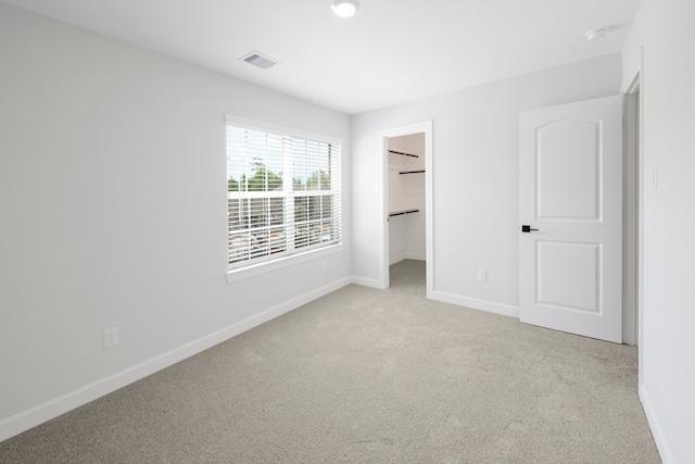 unfurnished bedroom with a walk in closet, a closet, and light colored carpet