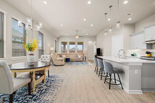 kitchen featuring white cabinetry, hanging light fixtures, a kitchen bar, decorative backsplash, and ceiling fan with notable chandelier