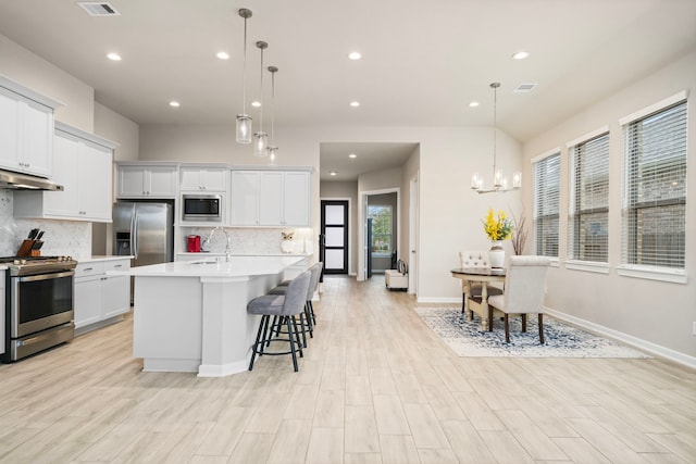 kitchen featuring pendant lighting, a kitchen island with sink, appliances with stainless steel finishes, and an inviting chandelier