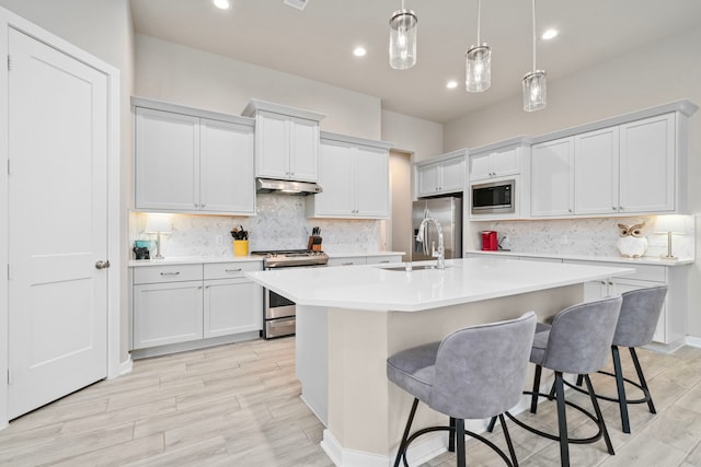 kitchen featuring a center island with sink, pendant lighting, a breakfast bar area, and appliances with stainless steel finishes