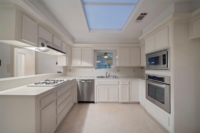 kitchen with a skylight, white cabinetry, sink, stainless steel appliances, and kitchen peninsula