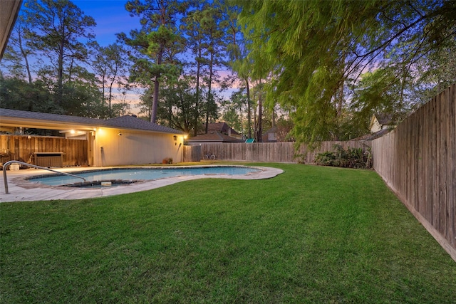 yard at dusk featuring a swimming pool with hot tub