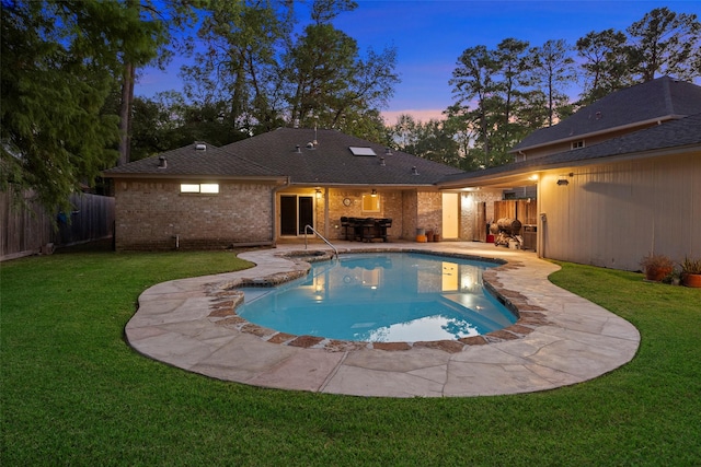 pool at dusk with a patio and a lawn