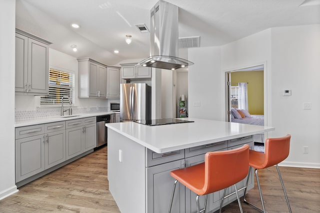 kitchen with island range hood, a breakfast bar area, appliances with stainless steel finishes, gray cabinetry, and a center island